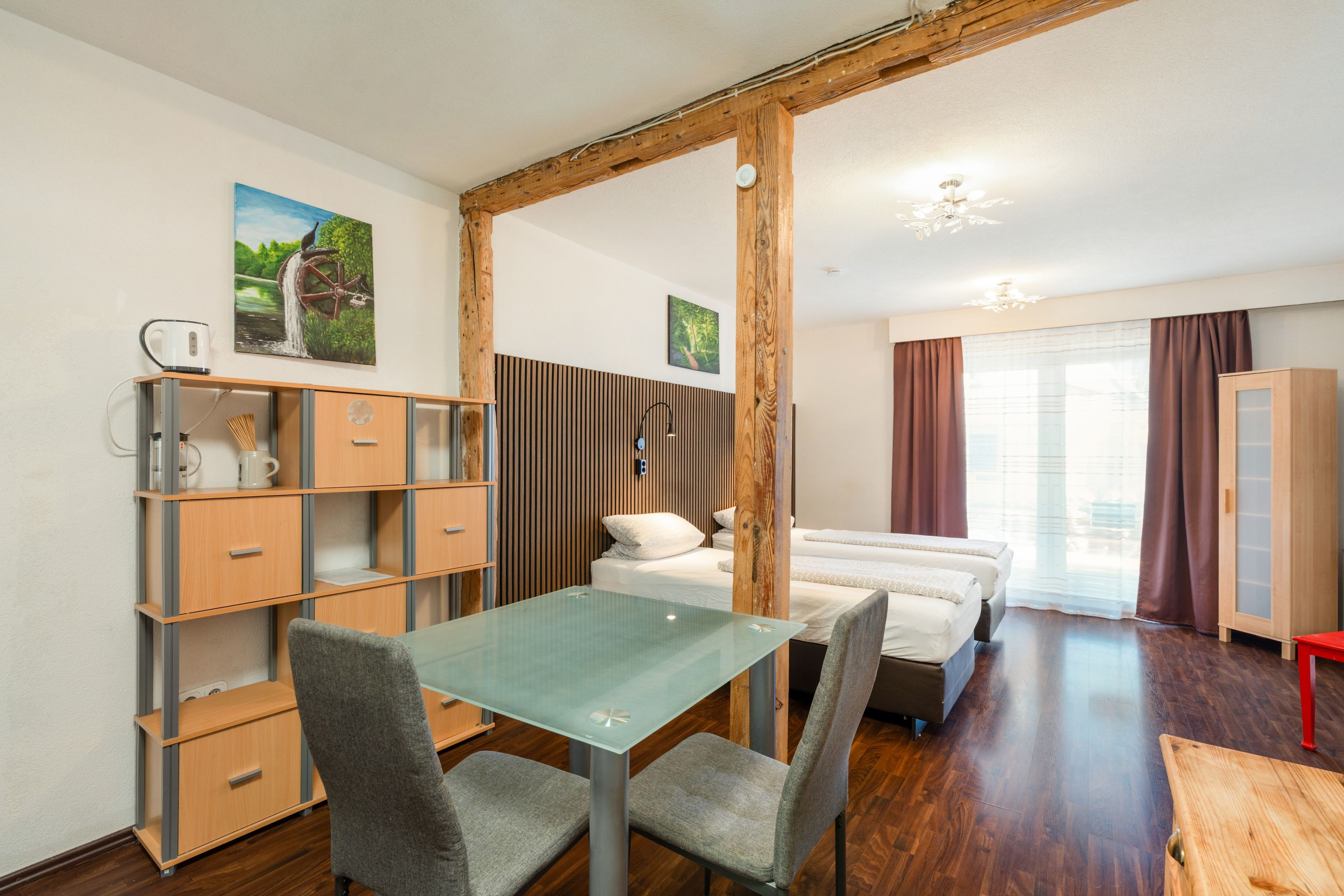 Hotellihuone, jossa on sänky, työpöytä tuoleineen, vaatekaappi ja taulu seinällä.