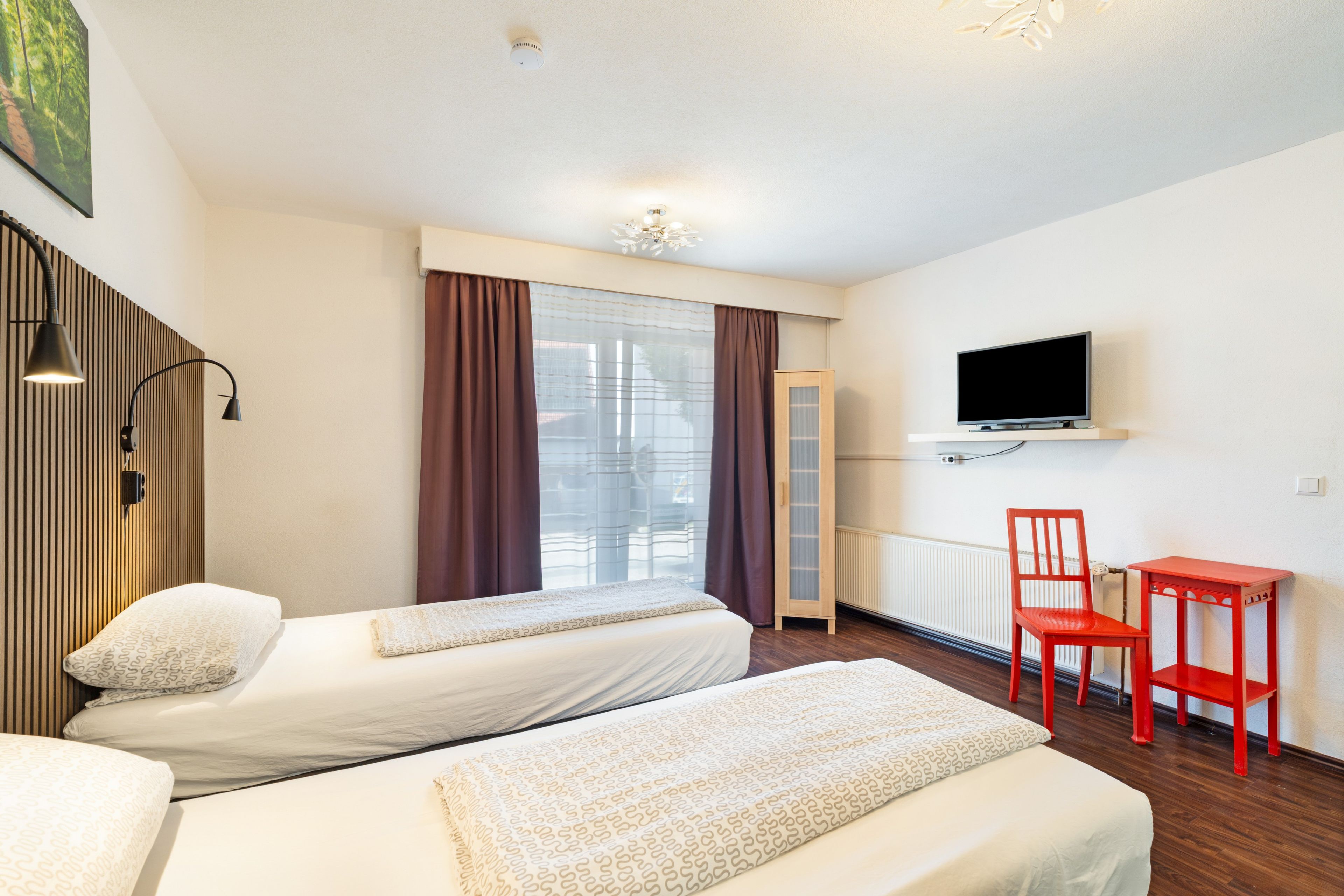 Ein Hotelzimmer mit zwei Betten, einem Fernseher, einem Schreibtisch und einem Sessel.