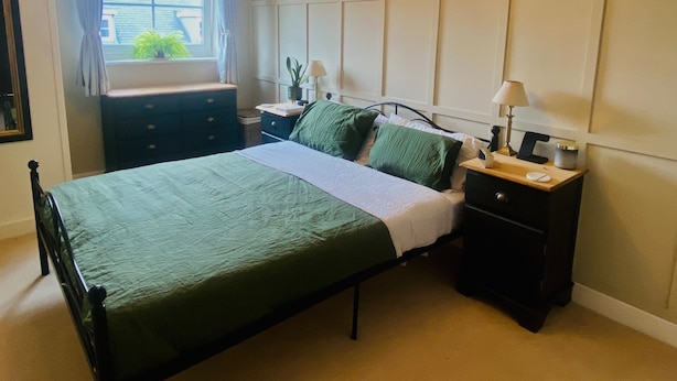 A bedroom with a bed, bedside tables, a window with curtains, and a wall panel design. - Apartment Sleeps 4 With Parking (Redhill)
