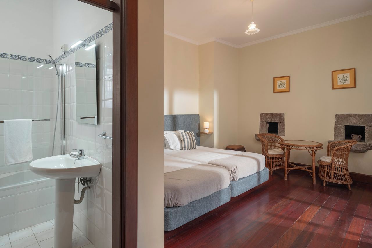 Ein Hotelzimmer mit Badewanne, einem Bett mit Kopfteil, einem Nachttisch, einem Korbstuhl und einem Kamin.