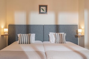 Ein Doppelbett mit zwei Kissen, ein gerahmtes Bild an der Wand und zwei Nachttischlampen.