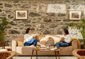 Ein gemütliches Zimmer mit einer Steinwand, zwei gerahmten Bildern, einem Sofa und einem Couchtisch mit einem Buch und einem Glas.