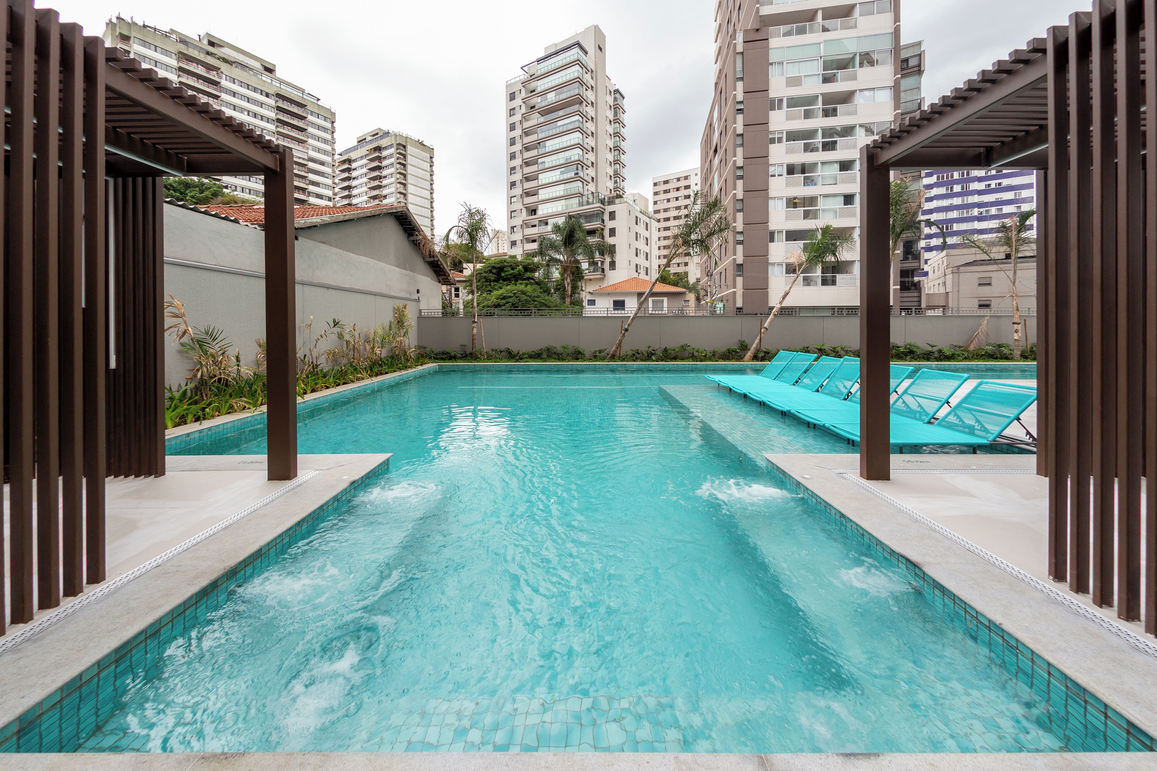 A swimming pool with clear water, surrounded by high-rise buildings, and a covered area with seating.