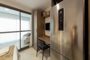 Ein modernes Hotelzimmer mit großem Fenster, einem Bett, einem Schreibtisch und einem eingebauten Kühlschrank.