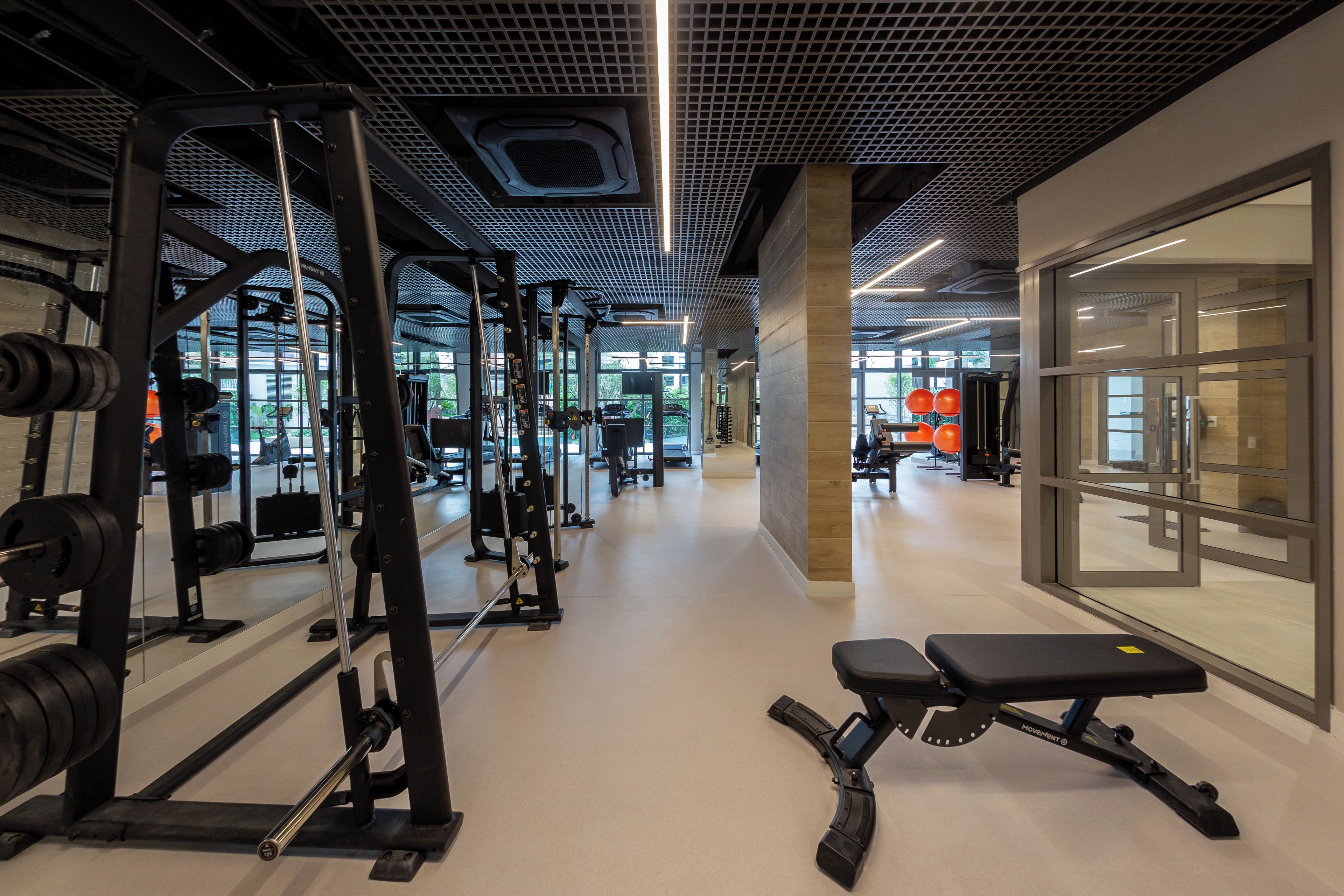 Ein Fitnessraum mit unterschiedlichen Trainingsgeräten, einer Bank und einer Wand mit einem Fenster.