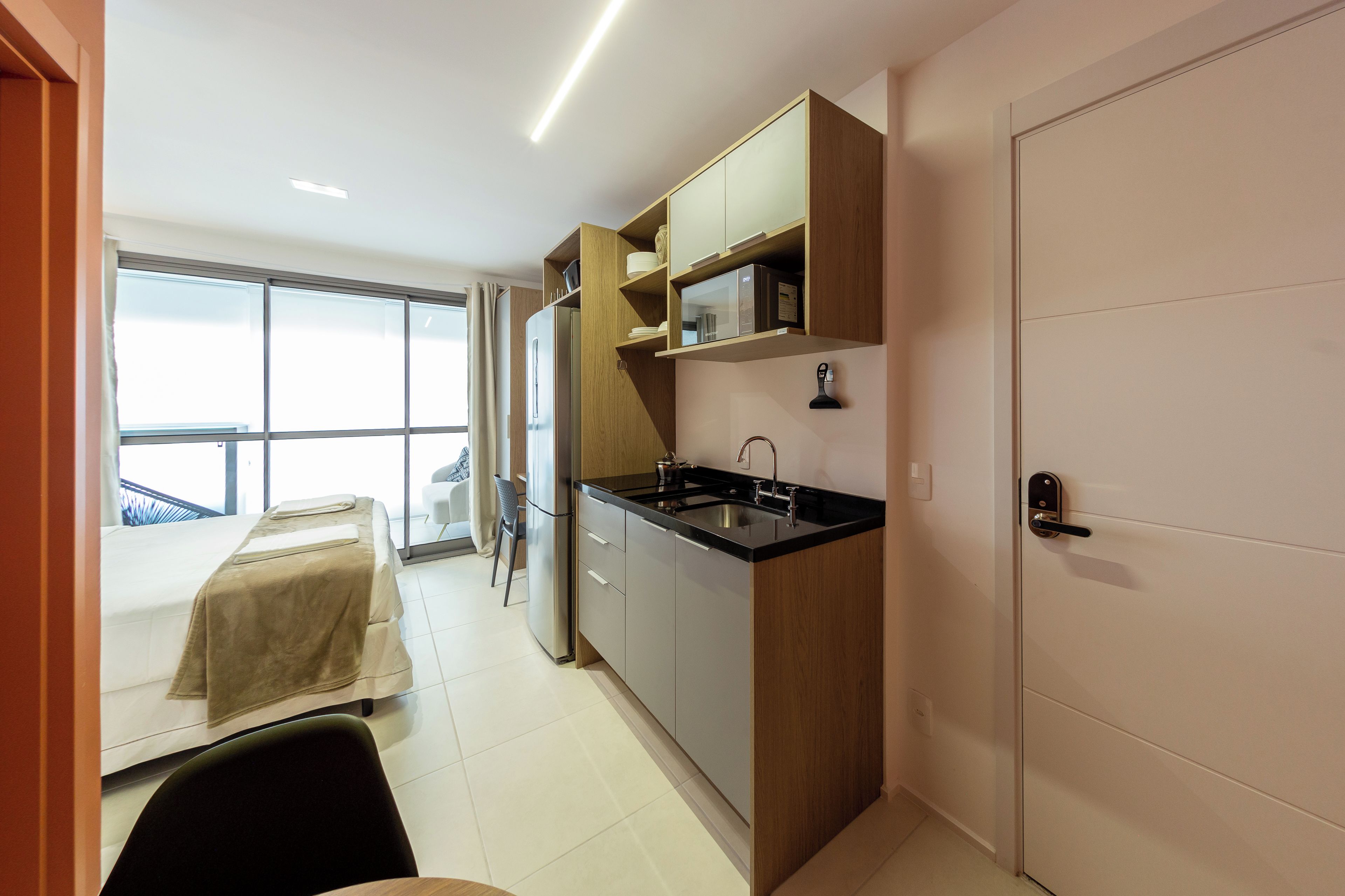 Una cocina moderna con refrigerador integrado, un lavamanos y armarios de madera. Hay una zona de comedor con mesa y sillas, y un ventanal que proporciona luz natural.