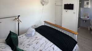 Una camera da letto con un letto, una ventola a soffitto, un armadio e un bagno visibile attraverso una porta aperta.