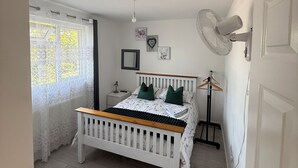 Una camera da letto con un letto, un comodino, una lampada a sospensione, una ventola a parete e una finestra con tende.