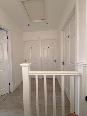 A hallway with white doors numbered 1 to 3, a white railing, and a tiled floor. - Roys House (Oxford)