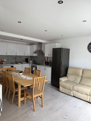 A modern kitchen with white cabinets, a black refrigerator, and a dining table with chairs. - Roys House (Oxford)