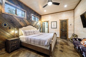 A bedroom with a large bed, wooden walls, a ceiling fan, and a window. - 4 King Suites | Hot Tub & Game Room (Broken Bow)