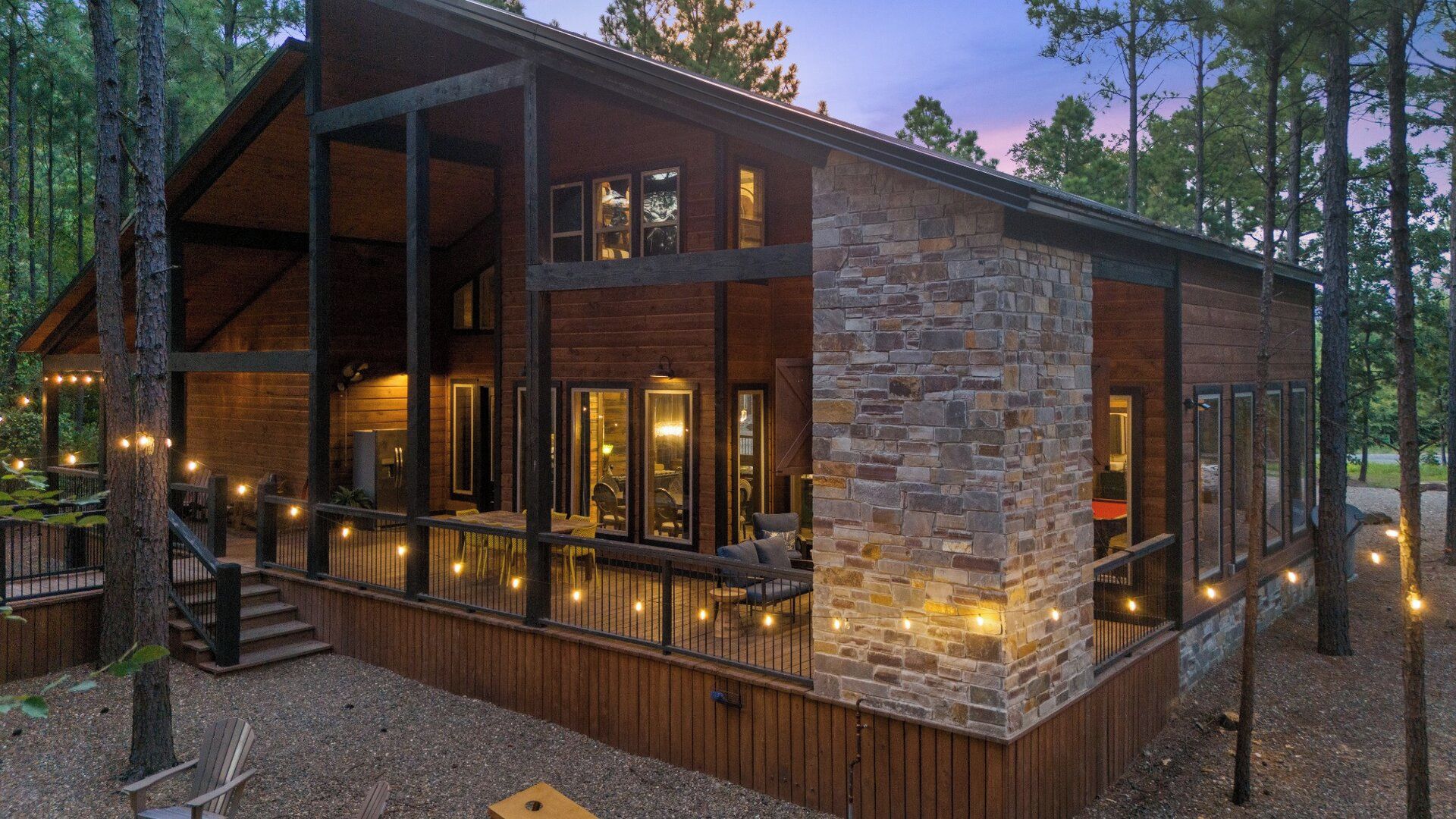 Une cabane avec une façade en pierre, de grandes fenêtres et une terrasse décorée de guirlandes lumineuses.