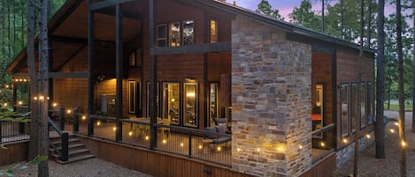 A cabin with a stone exterior, large windows, and a deck with string lights.