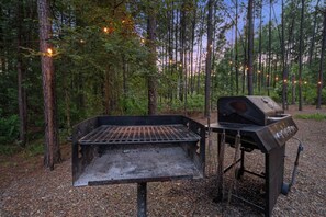 Ein tragbarer Grill ist in einer bewaldeten Gegend mit Bäumen und blauem Himmel aufgebaut.