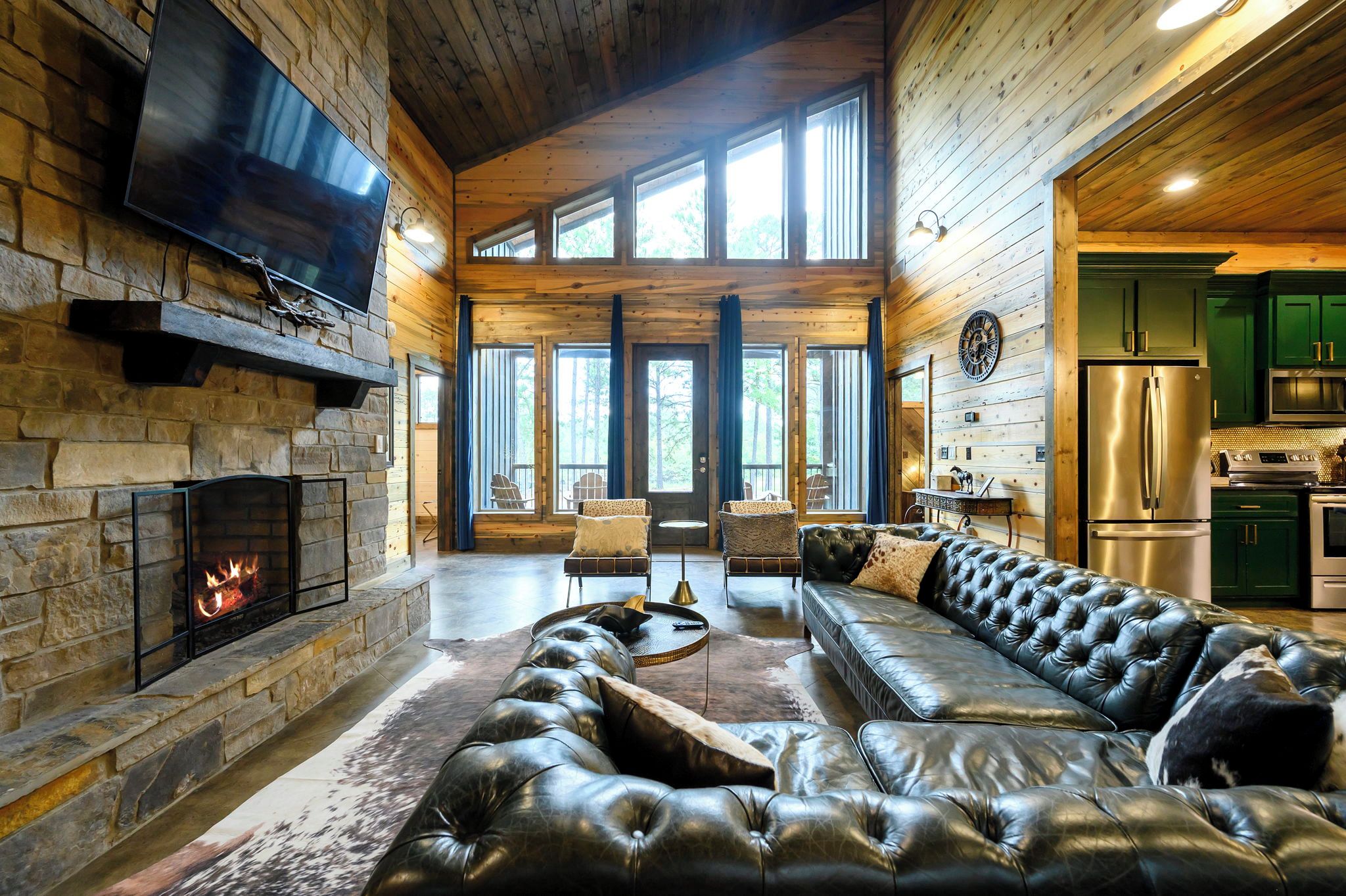 A log cabin interior with a stone fireplace, leather sofa, and a kitchen area.