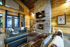 Ein Blockhaus-Interieur mit Kamin aus Stein, Ledersofa und einem an der Wand befestigten Fernseher.