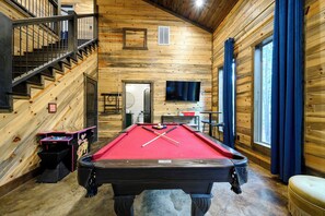 Ein Billardtisch in einem Holzraum mit Treppe und Fernseher.