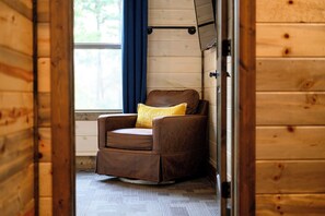 Ein gemütliches Zimmer mit einem braunen Ledersessel, einem gelben Kissen und einem Fenster mit blauen Vorhängen.