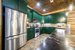 A modern kitchen with stainless steel appliances, green cabinets, and a marble countertop. - 4 King Suites | Hot Tub & Game Room (Broken Bow)