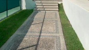 A modern building entrance with a concrete pathway leading to a door, a green fence on one side, and a clear sky. - Cozy 2BD ocean-front condo with tennis courts (Las Jarretaderas)