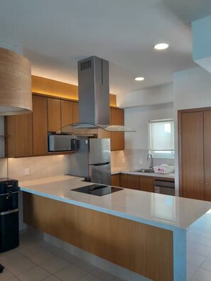 A modern kitchen with wooden cabinets, stainless steel appliances, and a central island. - Cozy 2BD ocean-front condo with tennis courts (Las Jarretaderas)