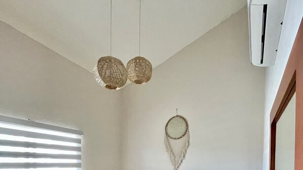 A hotel room with two beds, a bedside table, a lamp, a dreamcatcher, and a window with blinds. - Cozy 2BD ocean-front condo with tennis courts (Las Jarretaderas)