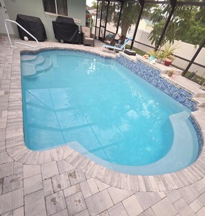 A swimming pool with a tiled edge, surrounded by a stone patio.