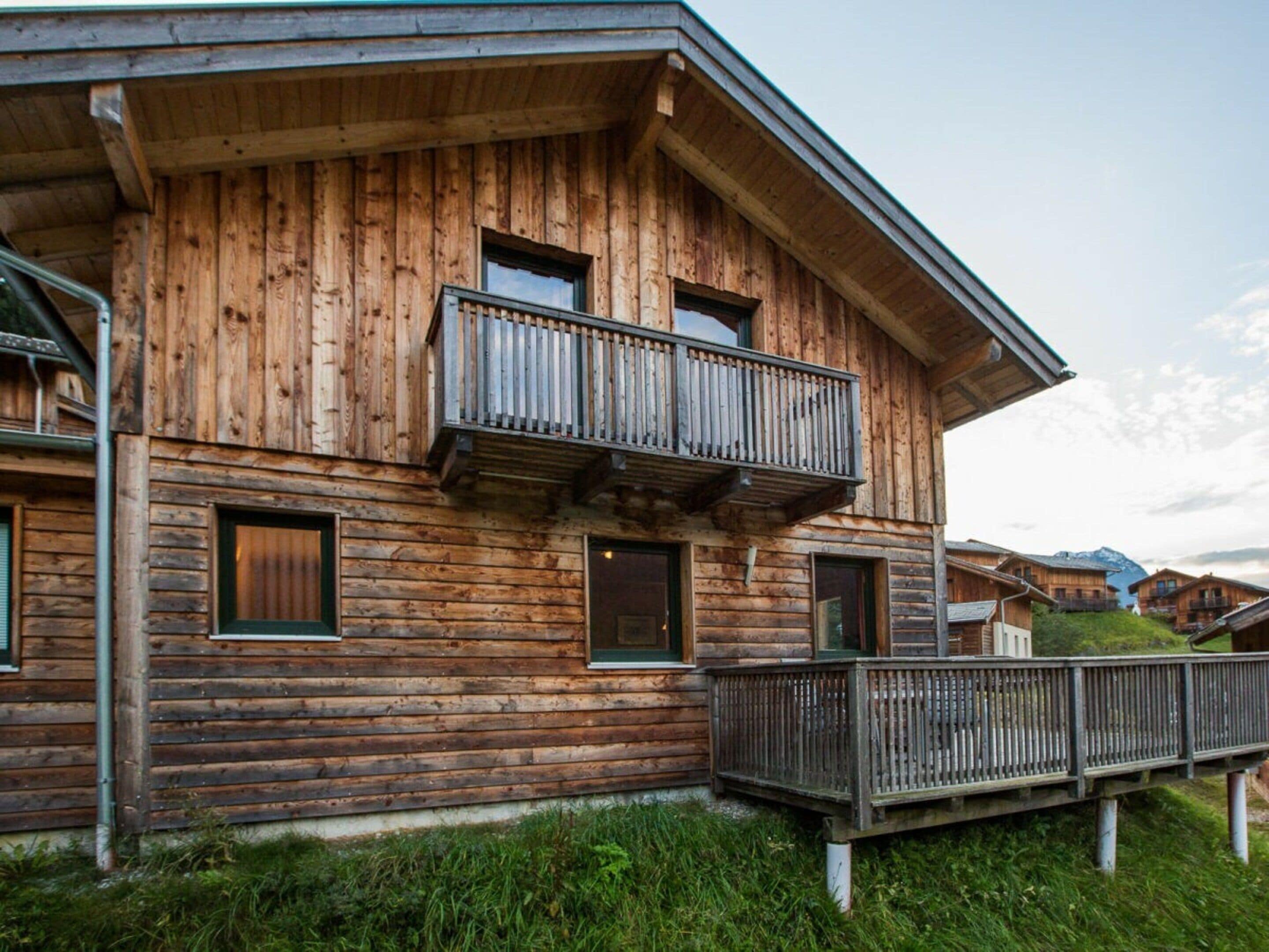 A wooden chalet with a balcony, a covered porch, and a view of the surrounding landscape.
