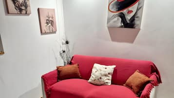 Un sofá rojo con dos almohadas, una alfombra floral y una obra de arte en la pared.