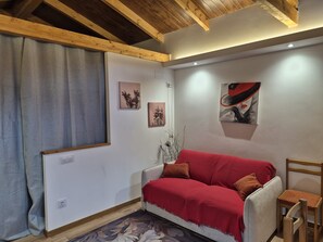 Une pièce chaleureuse avec un plafond en bois, un canapé rouge, une petite chaise en bois et deux tableaux accrochés au mur.