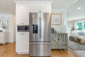 Ein Edelstahl-Kühlschrank von KitchenAid in einer modernen Küche mit weißen Schränken und einer darüberliegenden Mikrowelle.