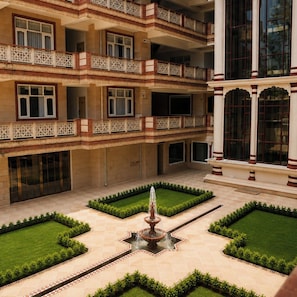 A courtyard with a central fountain, surrounded by neatly trimmed grass and geometric patterns.