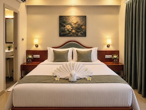 A hotel room with a bed, two bedside tables, a painting on the wall, and a bathroom visible through an open door.