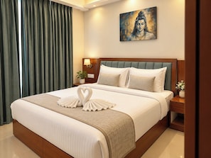 Une chambre d’hôtel avec un grand lit, une tête de lit, une table de chevet, une lampe, un tableau au mur et une fenêtre avec des rideaux.