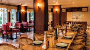 A long dining table with multiple chairs, set with plates and cutlery, in a room with wooden walls and ceiling. - Kamdhenu Lok (Haridwar)