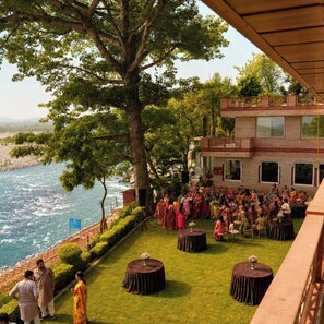 An outdoor event with a river view, a large tree, and a building with multiple windows.
