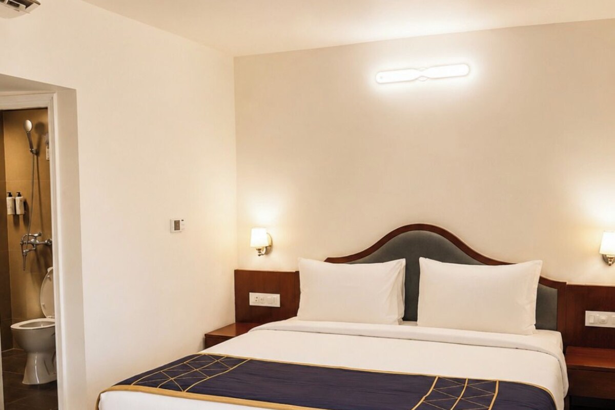 A hotel room with a bed, bedside tables, a nightstand, a wall-mounted light, and a door leading to a bathroom.