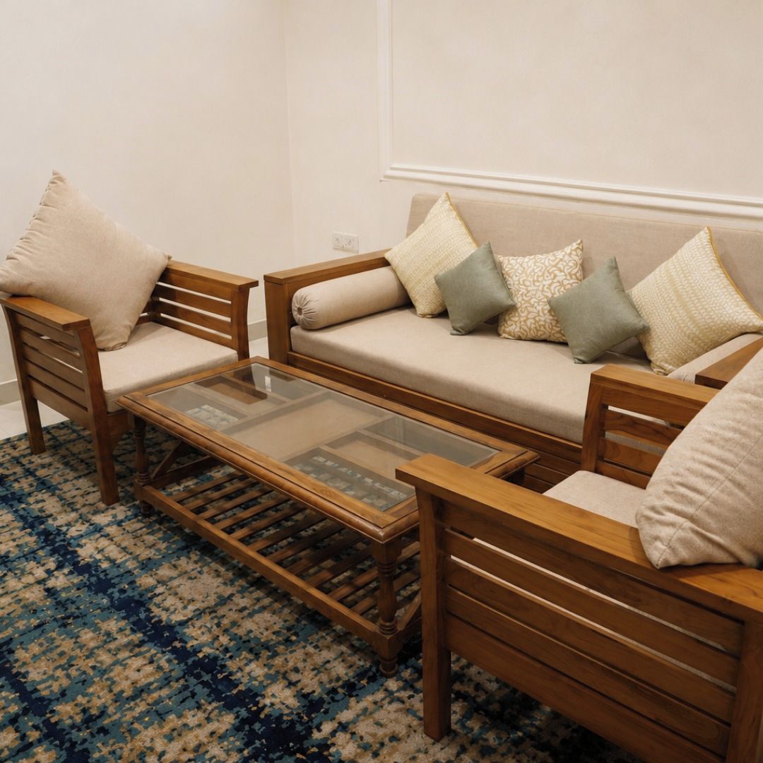 Una sala de estar con un sofá, dos sillas de madera, una mesa de centro de vidrio y un tapete estampado.