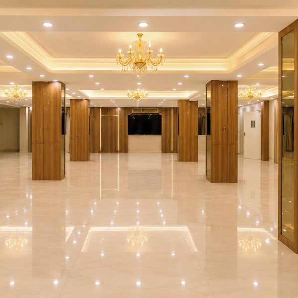 A spacious hotel lobby with a high ceiling, chandeliers, and wooden pillars.