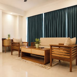 A living room with a sofa, two wooden chairs, a coffee table, and a potted plant.