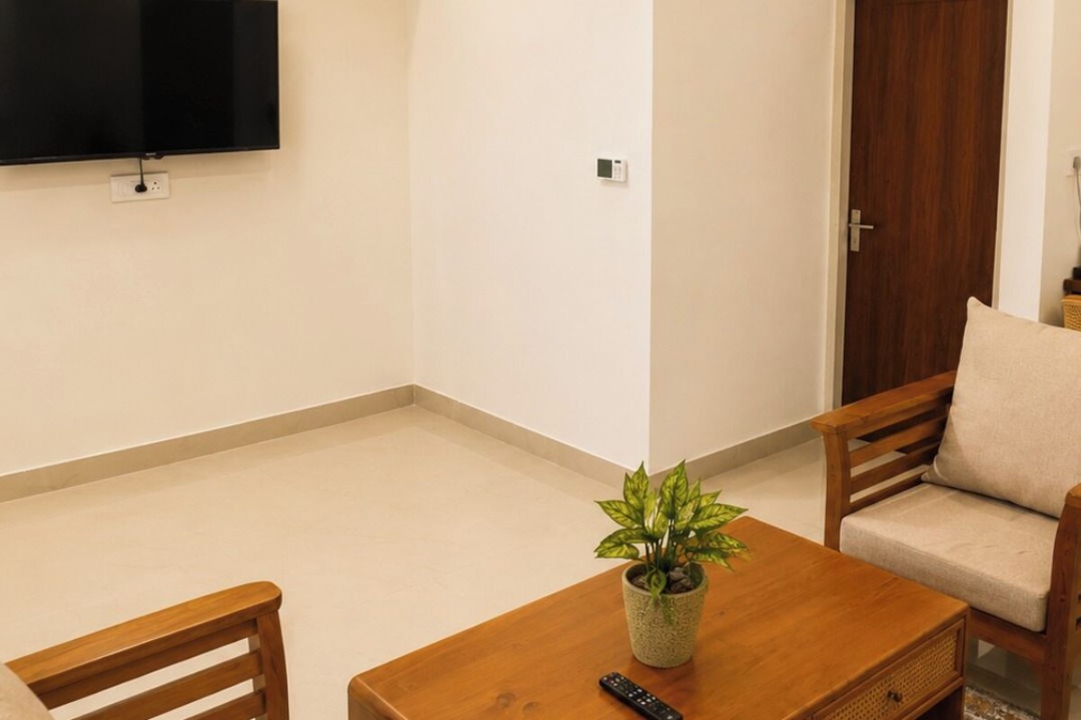 A living room with a flat-screen TV, ceiling fan, air conditioning unit, wooden furniture, and a potted plant.