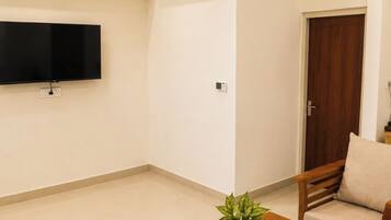 A living room with a flat-screen TV, ceiling fan, air conditioning unit, wooden furniture, and a potted plant.