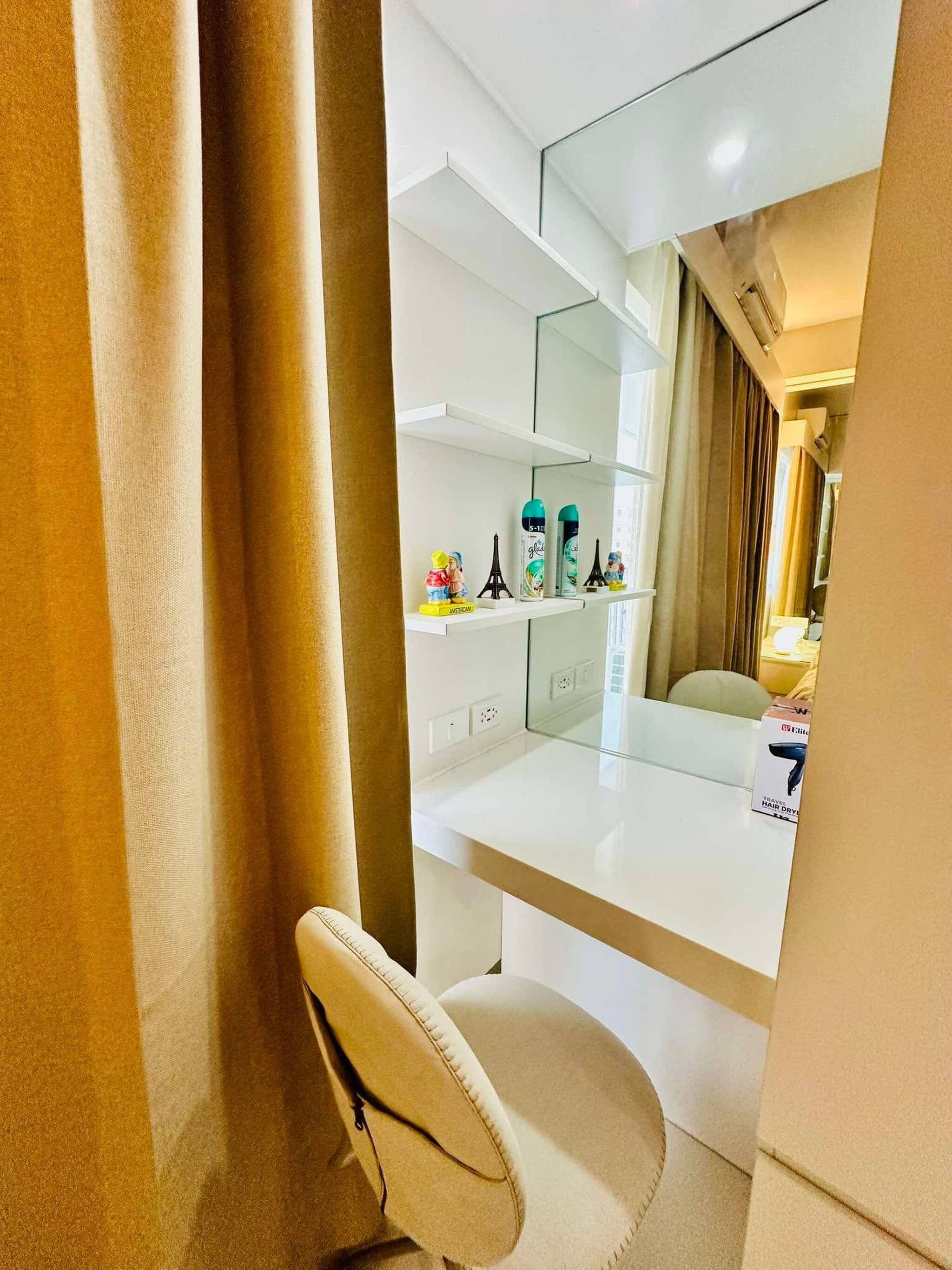 Une chambre d’hôtel avec un bureau blanc, une chaise, un miroir et une étagère contenant des articles de toilette et une petite figurine de la Tour Eiffel.