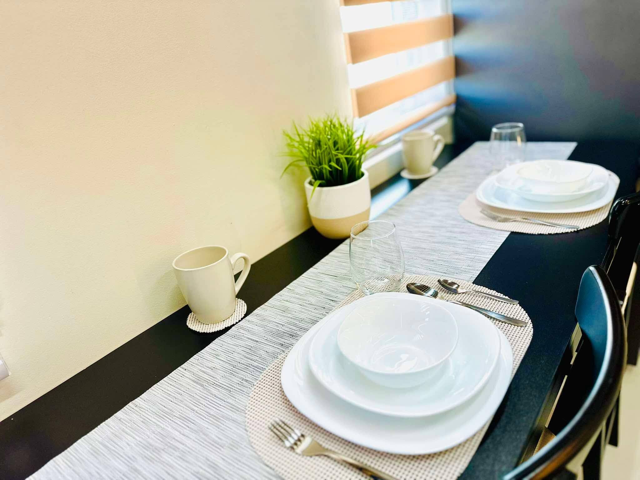Une table à manger dressée avec des assiettes, une tasse et un verre, avec une plante et un mur à rayures en arrière-plan.