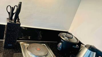 A kitchen with a black countertop, a stove with two burners, a kettle, and a pair of scissors in a holder.