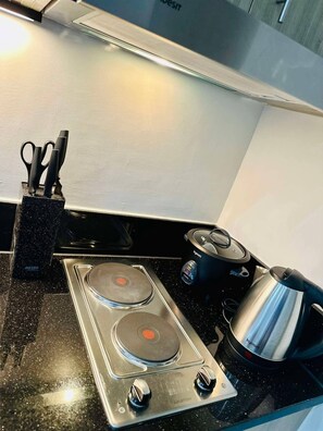 A kitchen with a black countertop, a stove with two burners, a kettle, and a pair of scissors in a holder. - Royal Fame Residence (Mandaluyong)