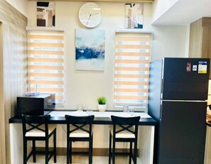 A kitchen with a dining table, chairs, a clock, and a refrigerator. - Royal Fame Residence (Mandaluyong)