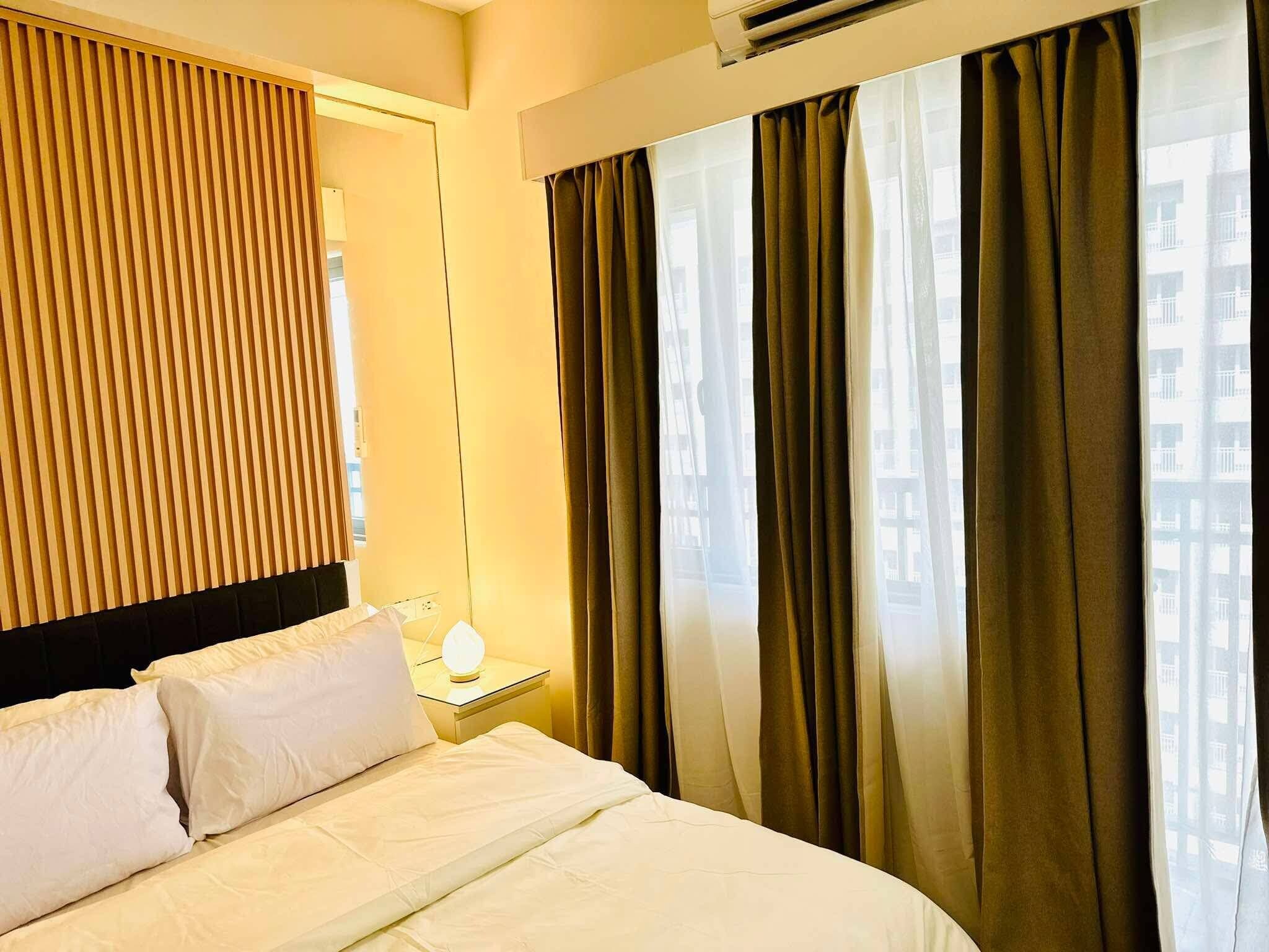 A hotel room with a bed, a nightstand, a lamp, and a window with curtains.