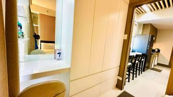 A hotel room with a bed, a chair, a desk, a mirror, and a kitchenette.