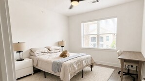 Un dormitorio con cama, lámparas de noche, un escritorio y ventana.